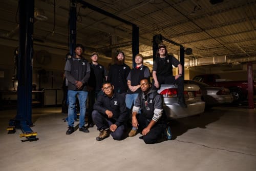 Group of automotive maintenance technician students standing around a car.